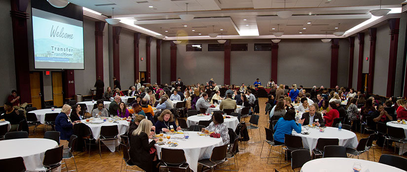 A group of advisors are gathered around several tables in a ballroom. 