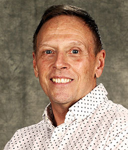 Art is pictured from the shoulders up wearing a white collared shirt with black polka dots. He has tan skin, dark hair, and is smiling. 