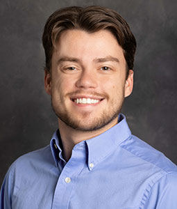 Rob is picture from the shoulders up wearing a blue collared shirt. He has brown hair and is smiling. 