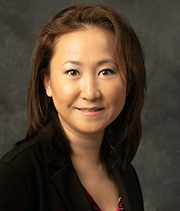 Mary Cha is pictured from the shoulders up wearing a black blazer. She has tan skin, short brown hair, and is smiling. 