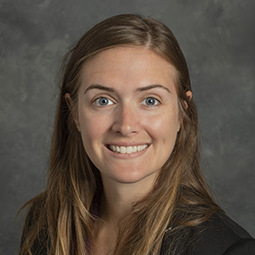 Rachel is pictured from the shoulders up wearing a back jacket. She has pale skin, blonde hair and is smiling. 