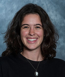 Allison is pictured from the shoulders up wearing a black shirt and necklace. She has shoulder length brown hair and is smiling. 