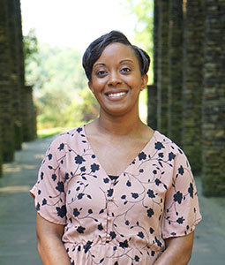 Chantelle is pictured from the waist up wearing a pick floral shirt. She has brown dark skin, black hair and is smiling. 