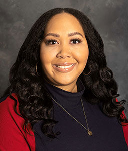 Alexis is pictured from the shoulders up wearing a black shirt and red jacket. She has tan skin, long black hair and is smiling. 