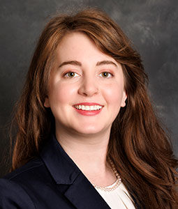 Brittany is pictured from the shoulders up. She has long brown hair and is smiling at the camera. 