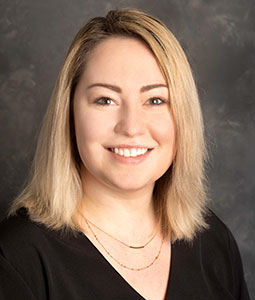 Alyssa is pictured from the shoulders up wearing a black shirt and gold necklace. She has short blond hair and is smiling. 