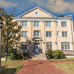 International House at Maxcy College is flanked by trees and shrub with a historic brick walk leading to the front entrance.