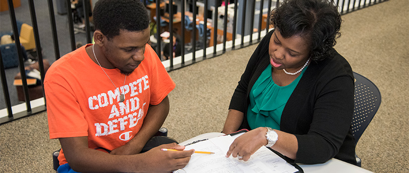 A male student in the library working with a Trio staff member.