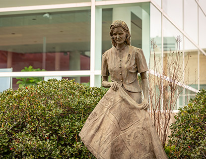 Statue of a woman holding a quilt in front of the Koger Center for the Arts.