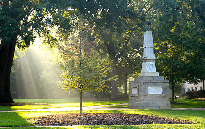 Lush green space of the historic horseshoe with the Maxcy Monument with sunshine streaming through the trees.