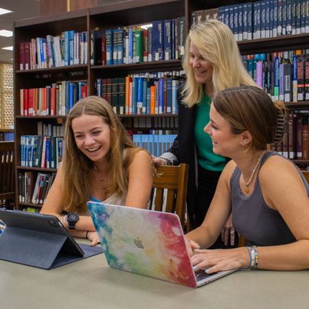 Two students and librarian converse and laugh while looking at a laptop computer.