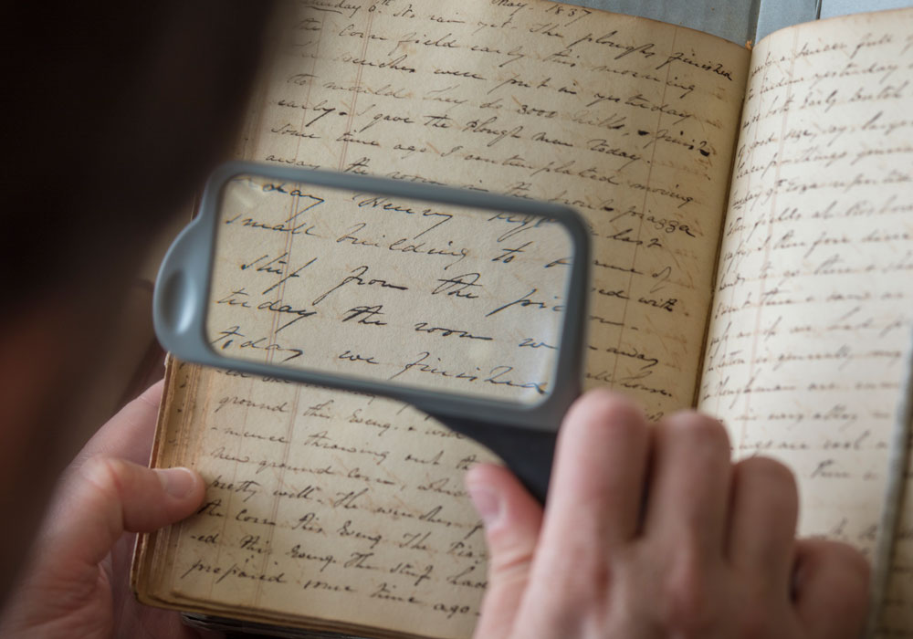 A person holding a magnifying glass examines a historical text.