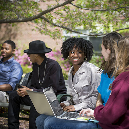 Student smiling and sitting on bench with laptop