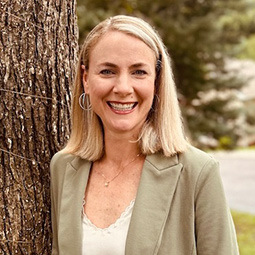 a woman outside smiling with a tan jacket and blonde hair