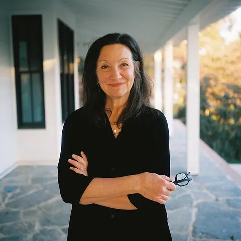 a woman in a black shirt smiles while standing on porch