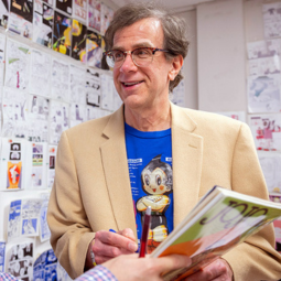 Media Arts professor Northrop Davis smiles at a student who is holding a manga/anime book.