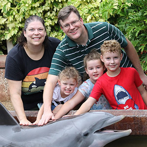 a family of two adults and three children petting a dolphin.