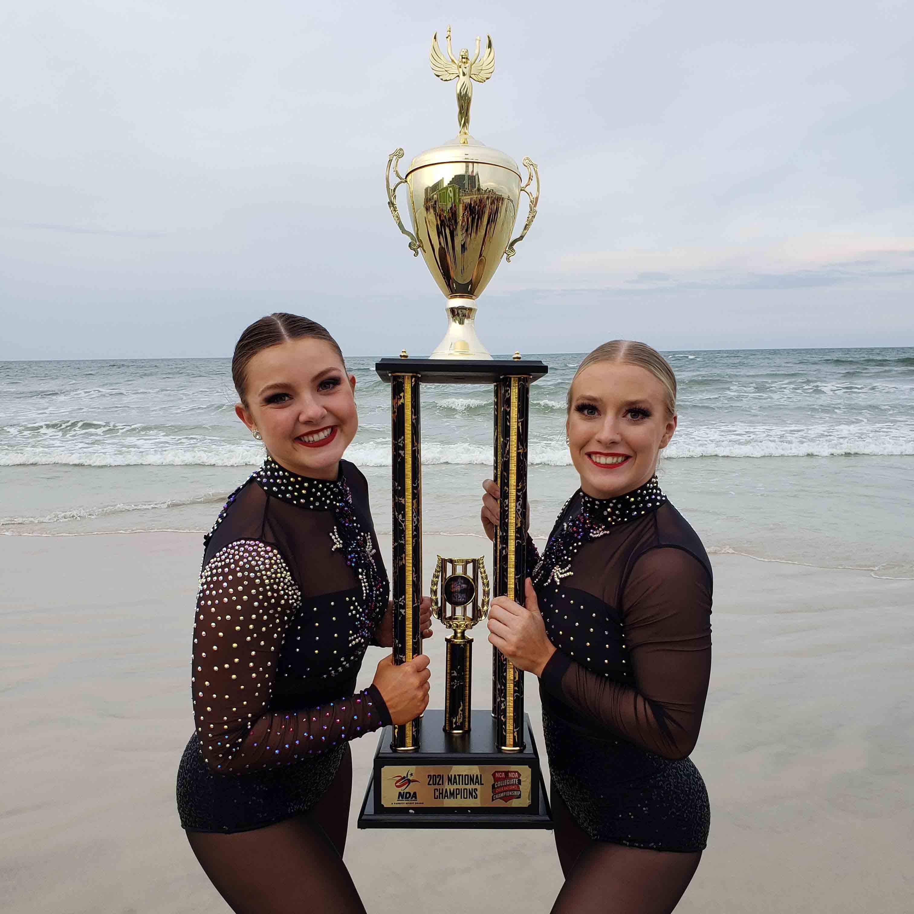 Two girls in dance uniforms holding trophey