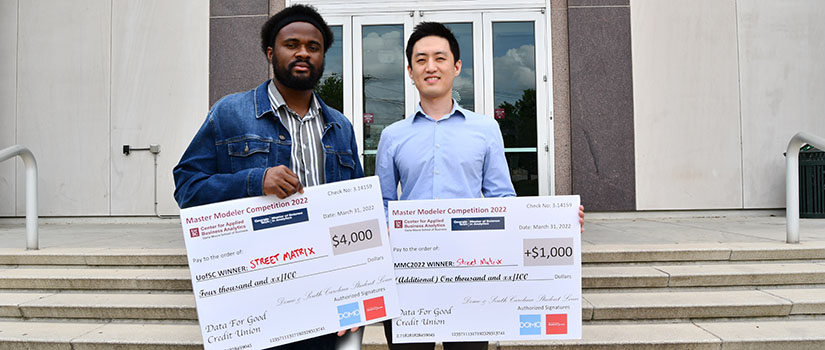 Two people holding large checks in front of the swearingen center