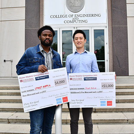 Two men holding large checks