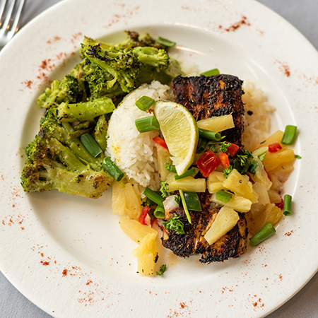 A plate of food with broccoli, rice and grilled pork with pineapples slices topped with a lime.