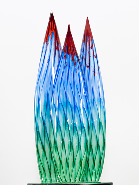 Abstract glass award featuring three elongated flame-shaped forms with blue and green textured glass and red accents at the tips, representing visionary leadership and innovation.