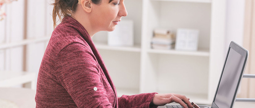 A woman with a hearing aid uses a laptop computer