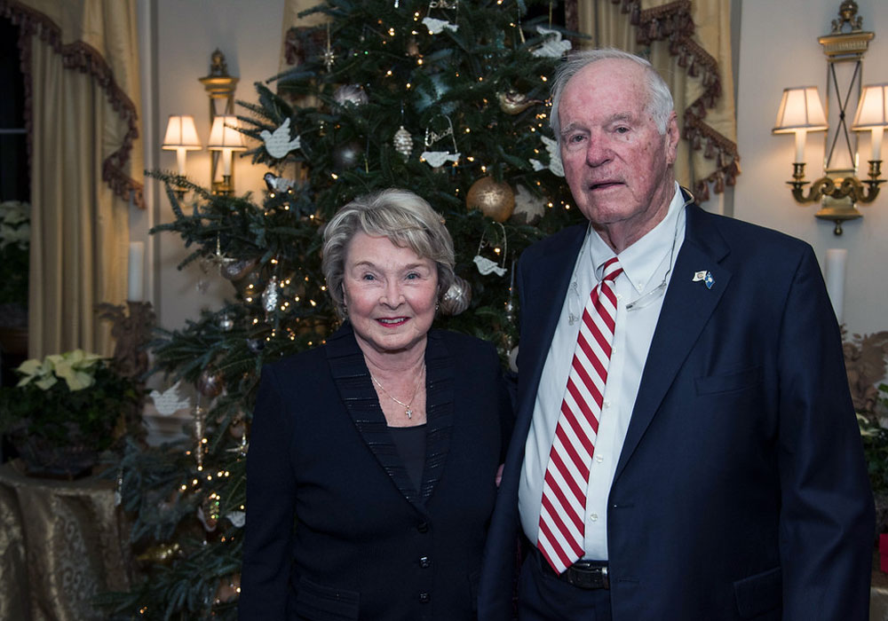 a man and woman stand in front of a christmas tree