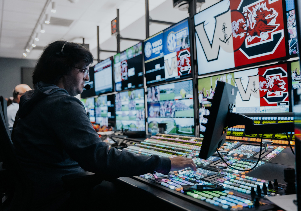 a person wearing a headset sits at a bank of TV screens