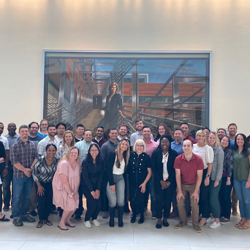 Students pose as a group in front of photo of Darla Moore at USC.