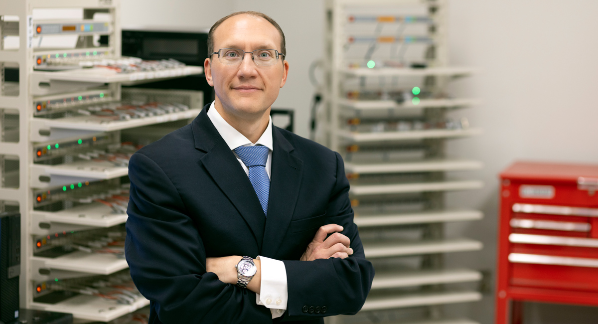 man stands with arms folded with lab equipment in the background