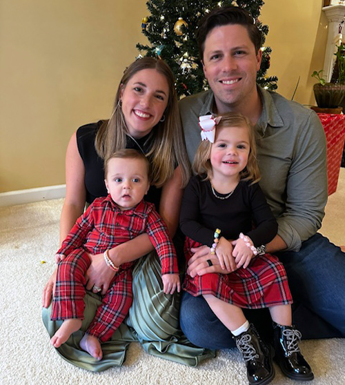 two people hold two children sitting in front of a christmas tree