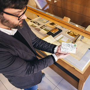 Michael Weißenburg holds a postcard above a display case.